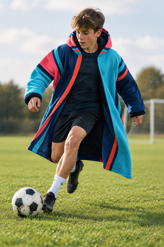 A hooded long coat shown from the back, featuring a bold geometric color-blocked pattern in light blue, dark navy, pink, and orange-red stripes, set against a plain white background.